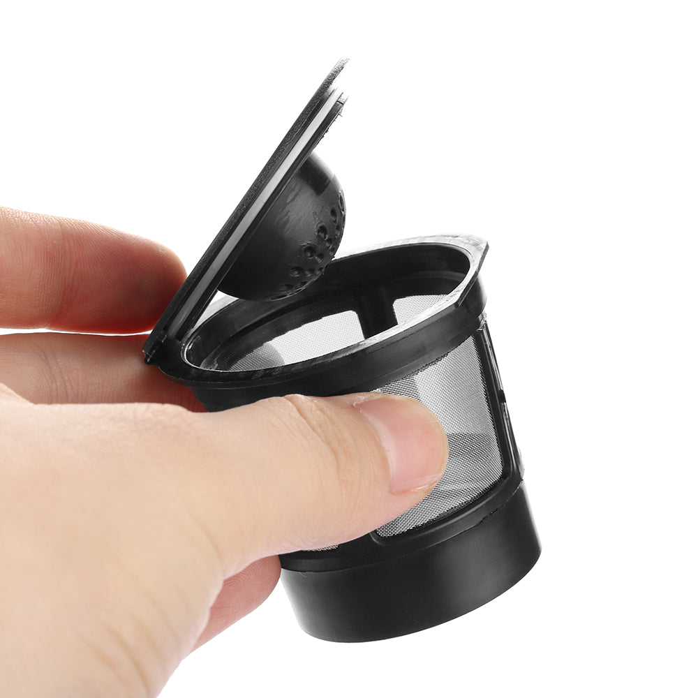 Hand holding a black reusable coffee filter with a mesh body and hinged lid, against a white background.