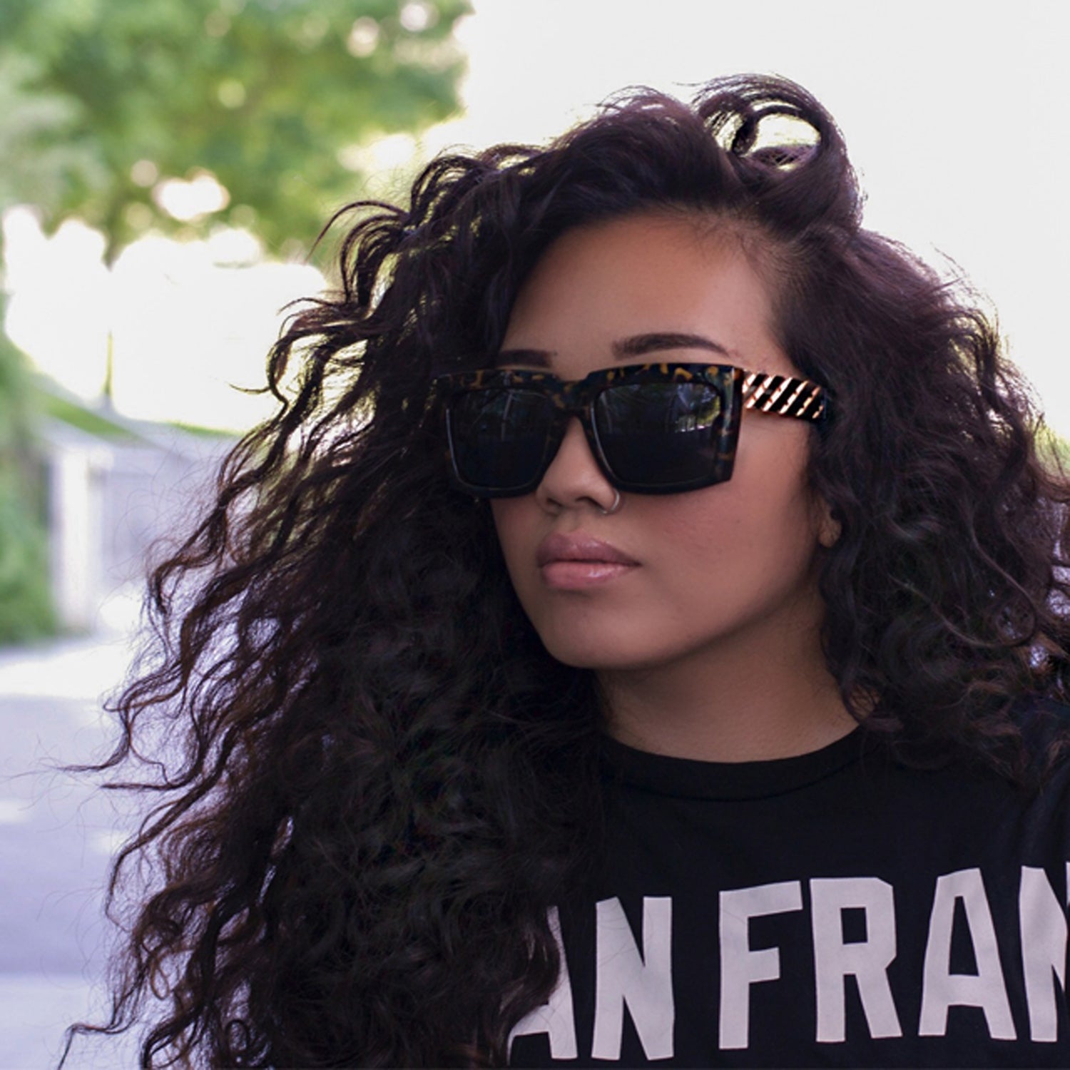 Person with curly hair, wearing tortoiseshell sunglasses and a black shirt with white text.