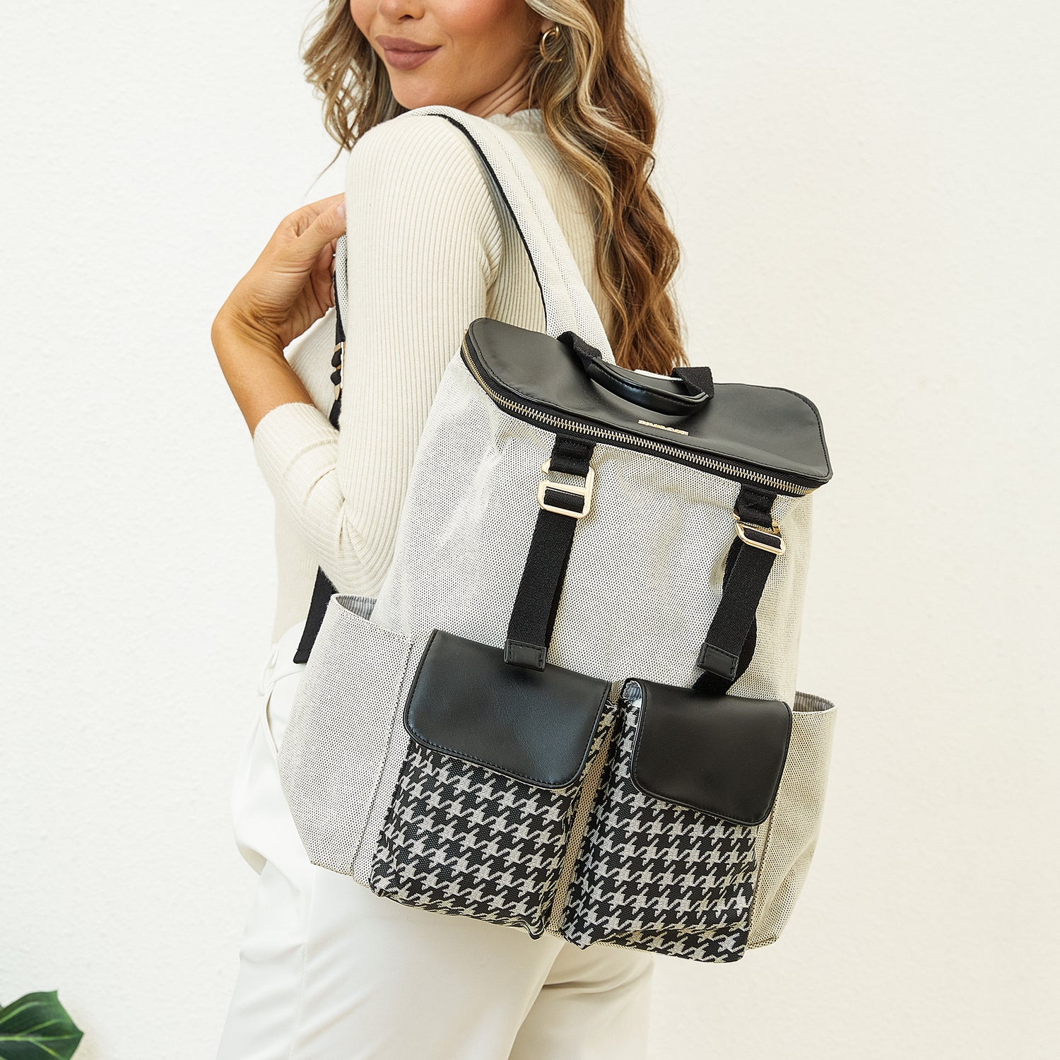 Woman with blond hair wearing a white outfit and carrying a houndstooth and black backpack.