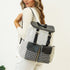 Woman with blond hair wearing a white outfit and carrying a houndstooth and black backpack.