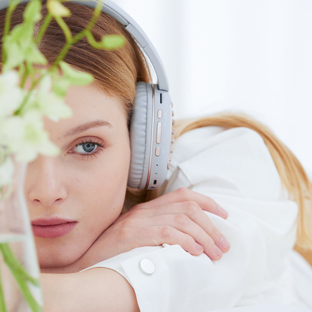 Woman in white with headphones, resting head on arms, soft focus flowers in foreground.