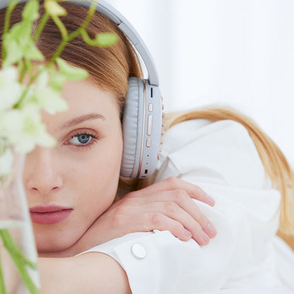 Woman in white with headphones, resting head on arms, soft focus flowers in foreground.