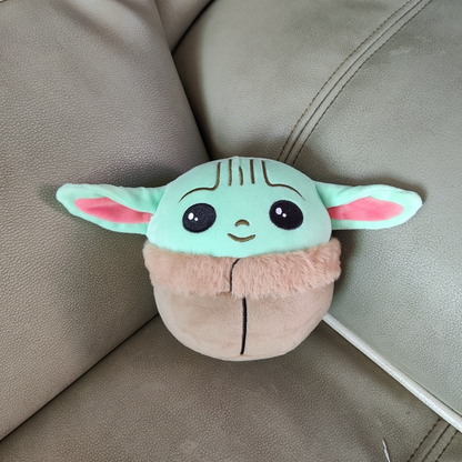 A plush toy with green ears, big eyes, and a fur collar, resting on a beige leather couch.