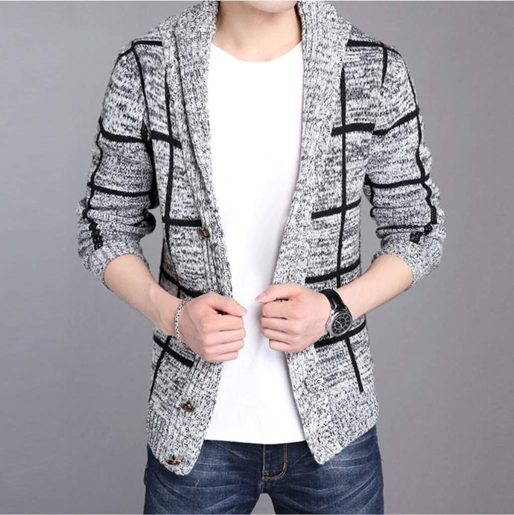 Man wearing a white shirt, gray-black patterned cardigan, and jeans, standing against a gray background.