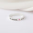 Silver ring with engravings, pink gem, and baby footprints on white background.