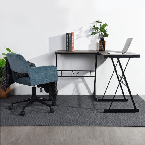 Gray desk with books, plant, and laptop; blue chair on dark rug; wood floor background.