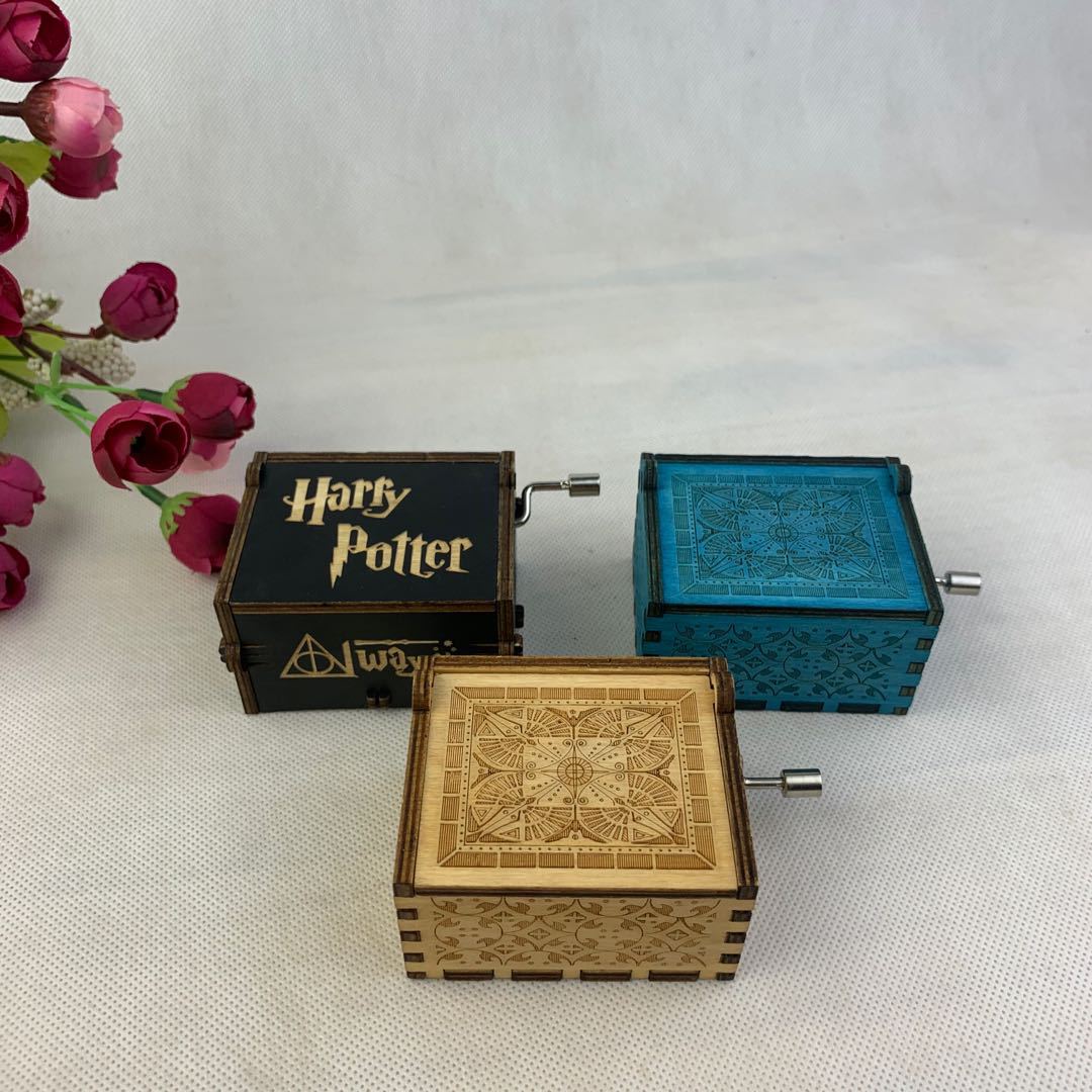 Three intricately carved music boxes in black, blue, and light wood, on a white surface with red flowers.
