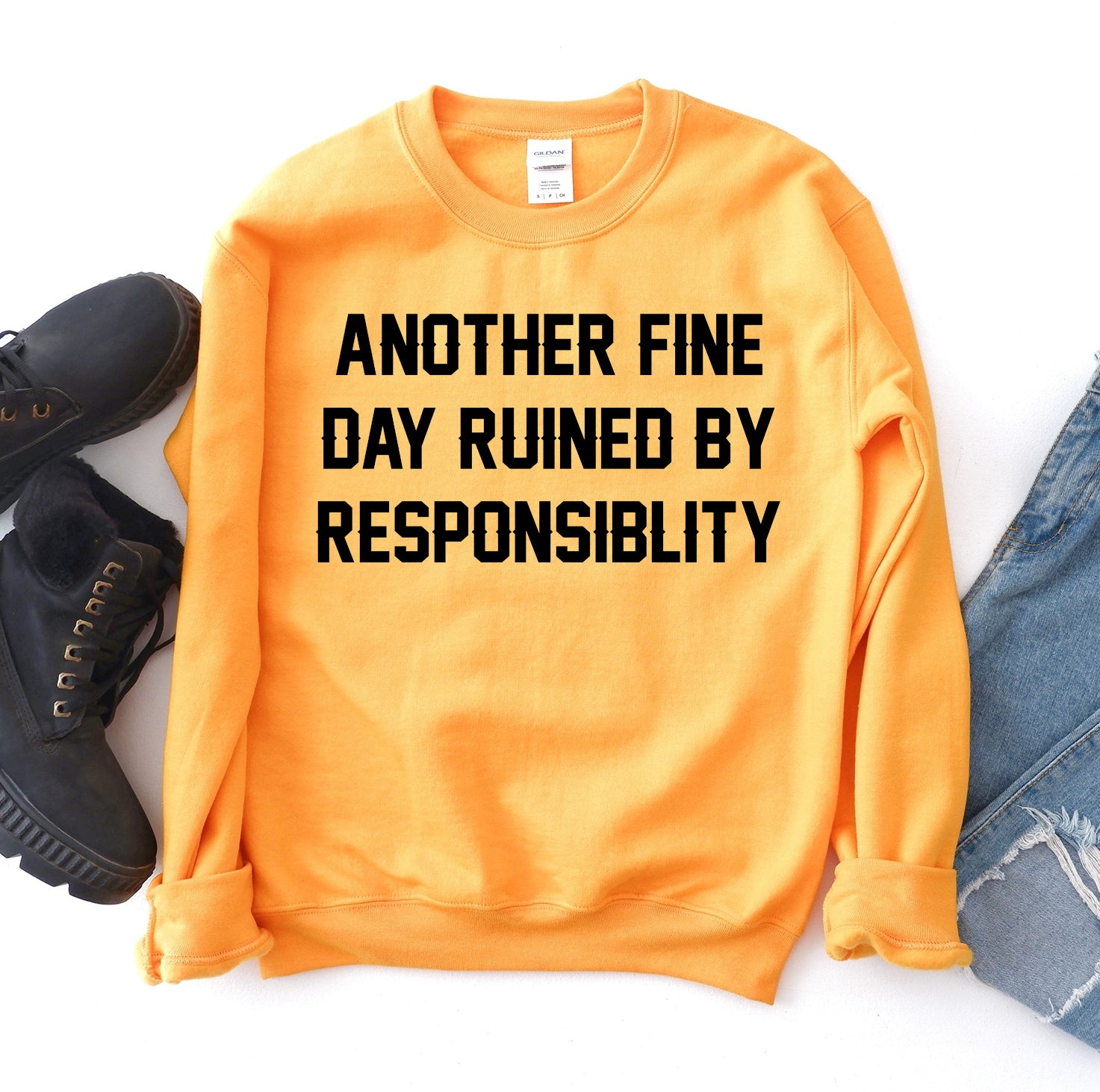 Orange sweatshirt with "Another fine day ruined by responsibility" text, next to black boots.