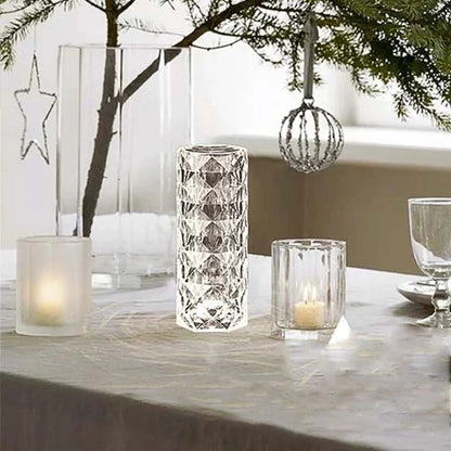 Elegant glassware on a table with candles, a hanging ornament, and green branches above.