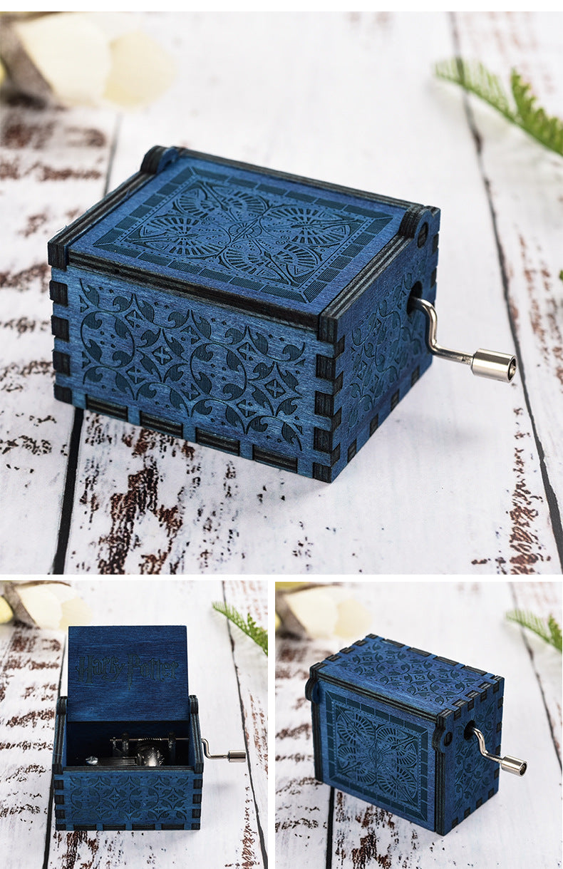 Blue engraved wooden music box with a side crank on a white rustic surface.