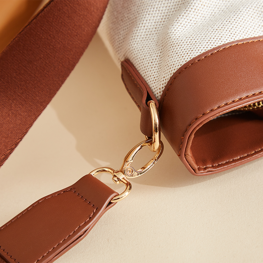 Brown leather bag with gold clasp and white fabric detail on beige surface.