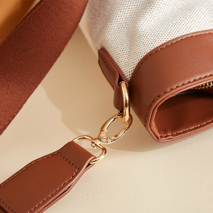 Brown leather bag with gold clasp and white fabric detail on beige surface.