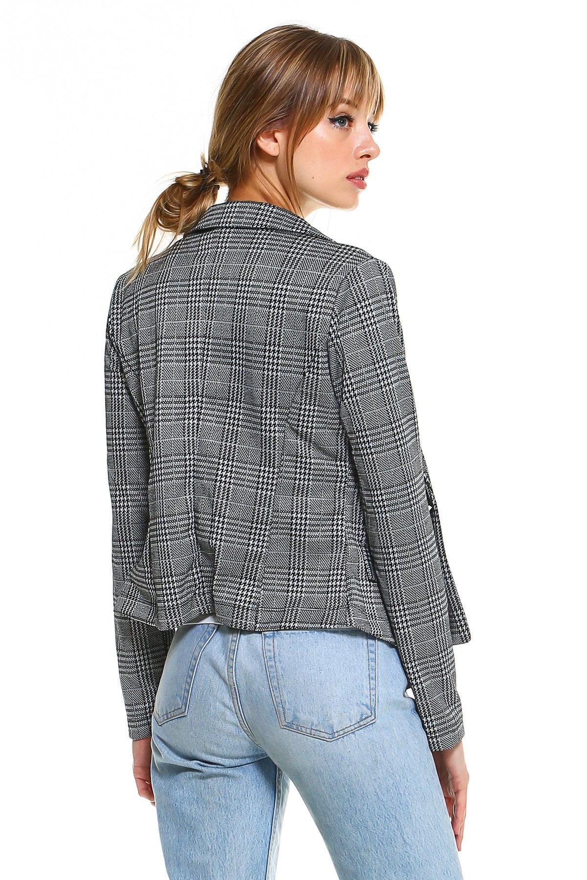 Woman in plaid blazer and light blue jeans, facing away, with hair in a loose ponytail.