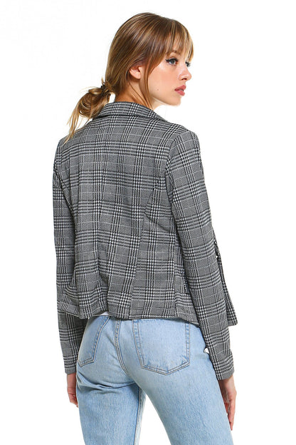 Woman in plaid blazer and light blue jeans, facing away, with hair in a loose ponytail.