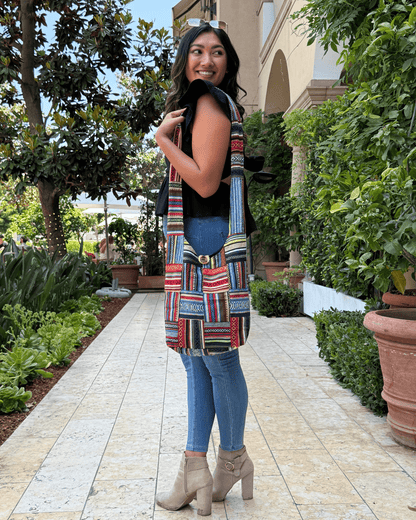 Woman in a garden, wearing blue jeans, tan boots, and colorful patterned jacket, smiling back.