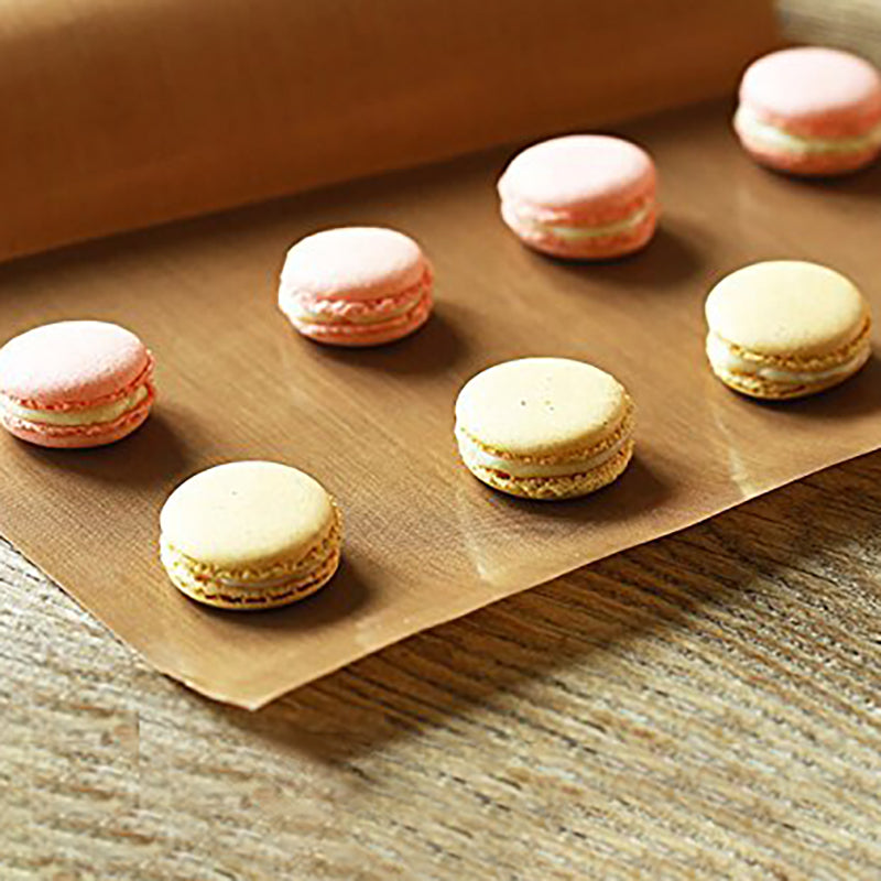 Pink and beige macarons on brown parchment paper, arranged neatly on a wooden surface.