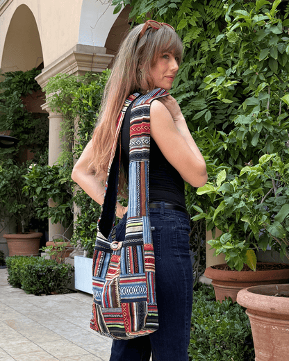 Woman with a colorful patterned tote bag stands in a leafy courtyard, wearing sunglasses on head.