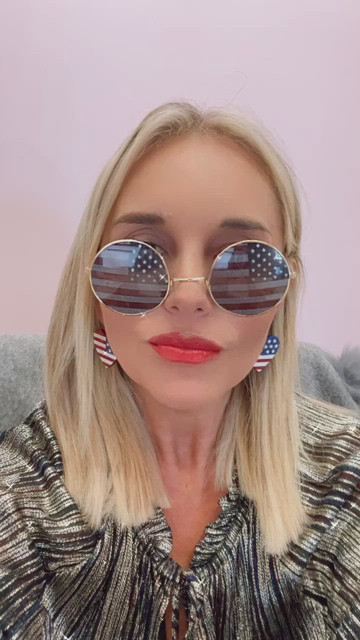 Woman with blonde hair, wearing sunglasses and earrings featuring the American flag design.