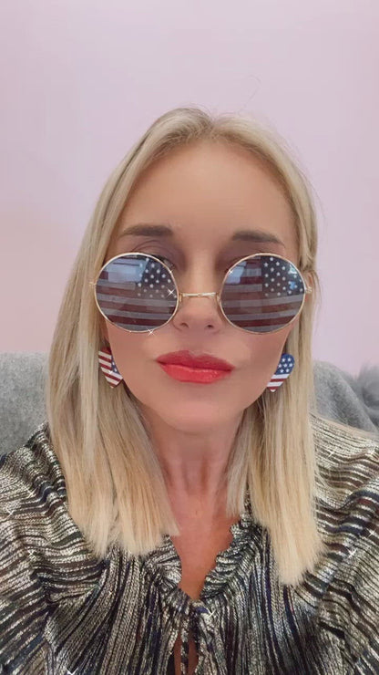 Woman with blonde hair, wearing sunglasses and earrings featuring the American flag design.