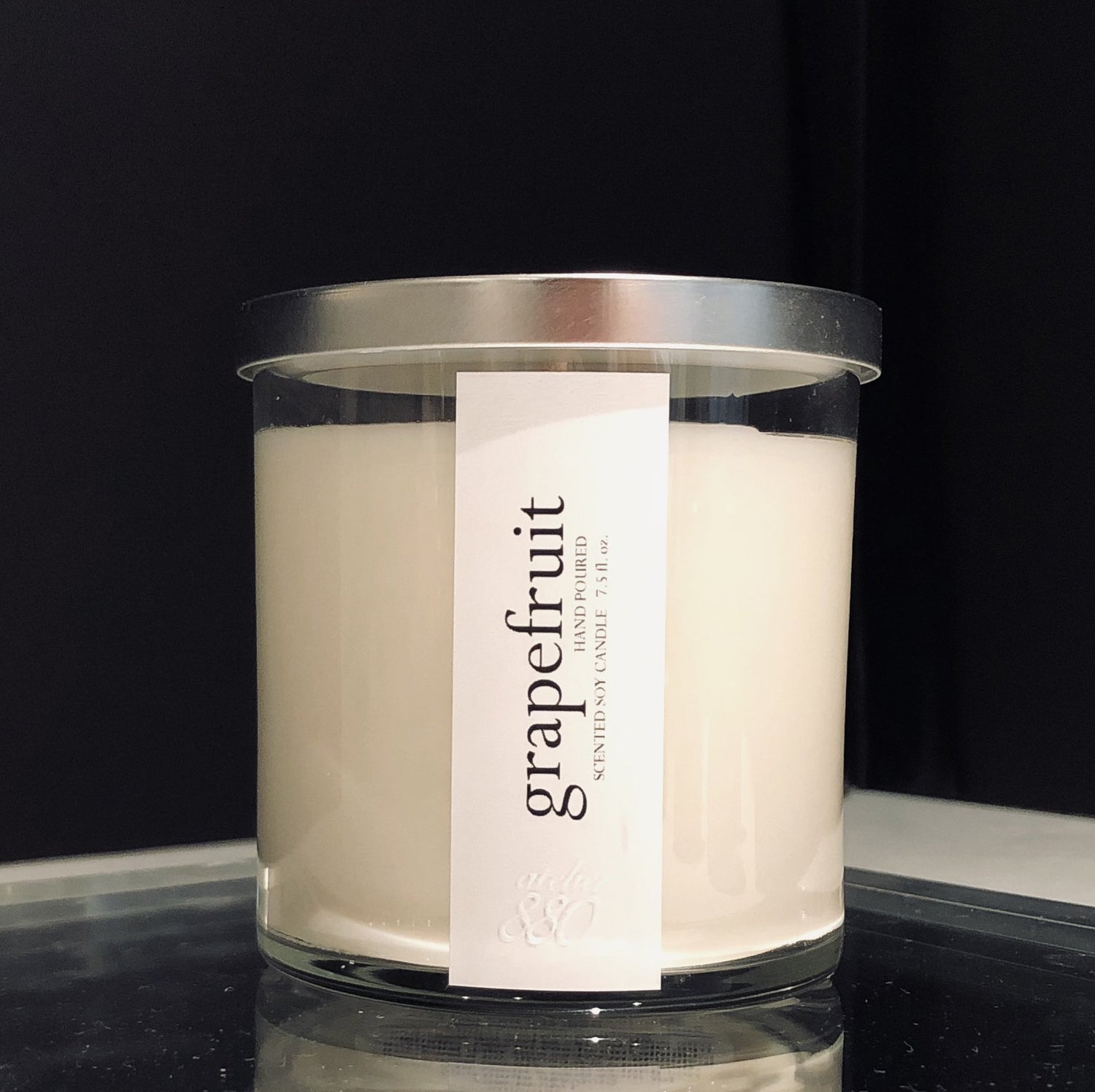 Glass jar candle with white wax, silver lid, and "grapefruit" label in black text.