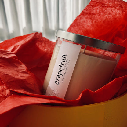 A grapefruit-scented candle with a silver lid, nestled in bright red tissue paper.