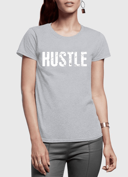 Woman in a light gray "HUSTLE" T-shirt with bold white text, wearing dark pants and jewelry.