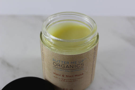 Open jar of yellow hair and nail mask on a marble surface, labeled "Butter Me Up Organics".