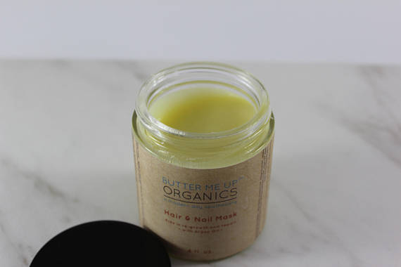 Open jar of yellow hair and nail mask with brown label, on a white marble surface.