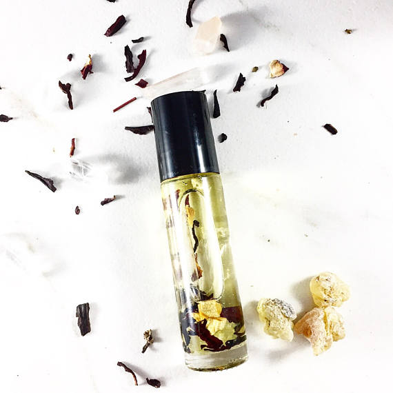 Clear bottle with black cap on white background, filled with oil and plant pieces, surrounded by herbs.