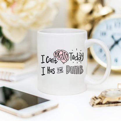White mug with text and a pink brain graphic, beside a smartphone and a blurred clock.