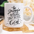 White mug with black cursive text: "The struggle is real, but so is God," on a gold coaster.