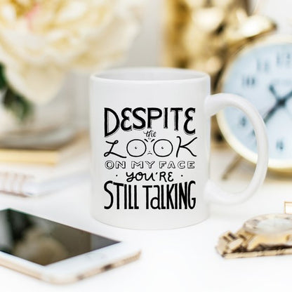 White mug with black text saying "Despite the look on my face, you&