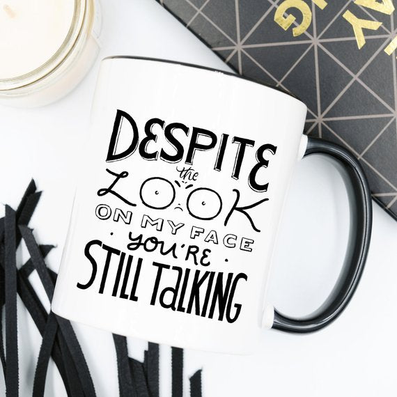 White mug with black handle, text reads "Despite the look on my face you&