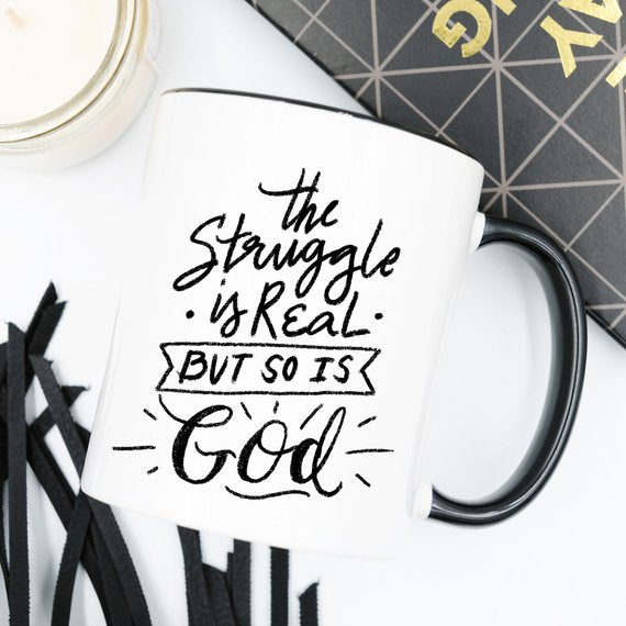 White mug with black handle and text: "The struggle is real, but so is God."