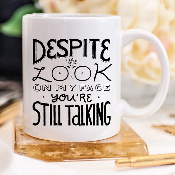 White mug with black text: "Despite the look on my face, you&