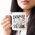 Woman holding a white mug with black text: "Despite the look on my face, you&