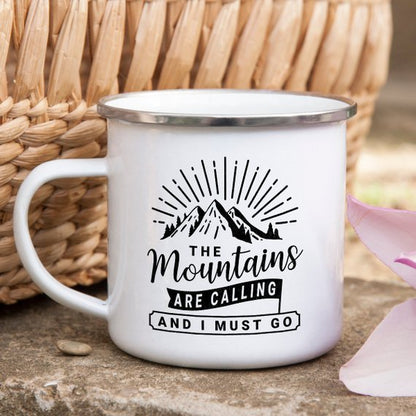 White enamel mug with mountain design, sun rays, and text "The Mountains are Calling and I Must Go."