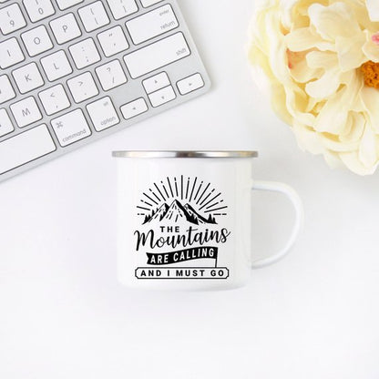 White mug with mountain design and text, next to a white keyboard and cream flower.