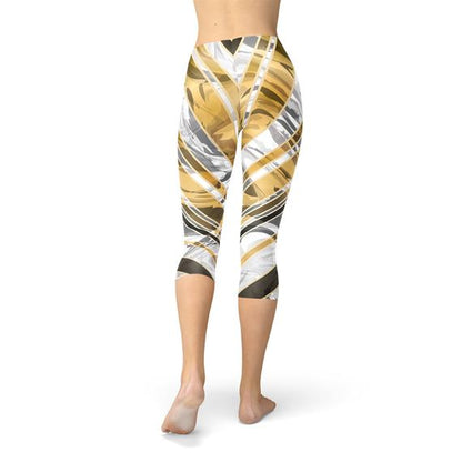 Woman wearing leggings with gold, white, and gray abstract patterns, standing barefoot.