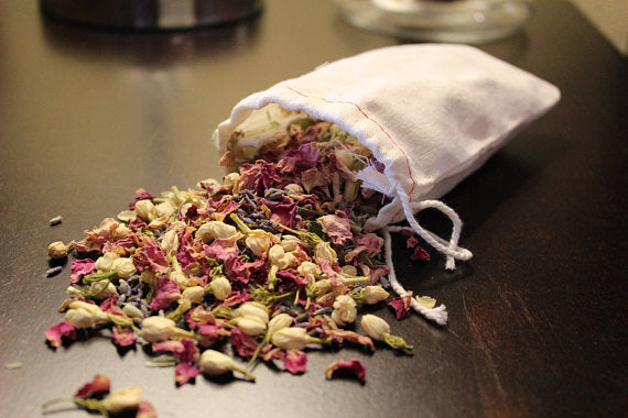 Dried flowers in pink, white, and green spill from a small, open white pouch onto a dark surface.
