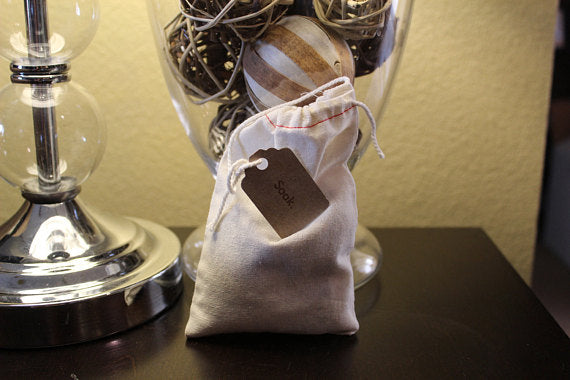 Small drawstring bag with a label on dark table, next to a glass lamp.