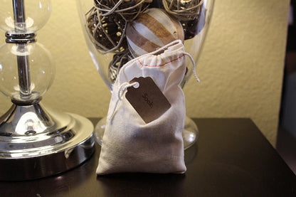 Small drawstring bag with a label on dark table, next to a glass lamp.