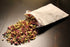 White pouch spilling dried colorful flower petals on a dark wooden surface.