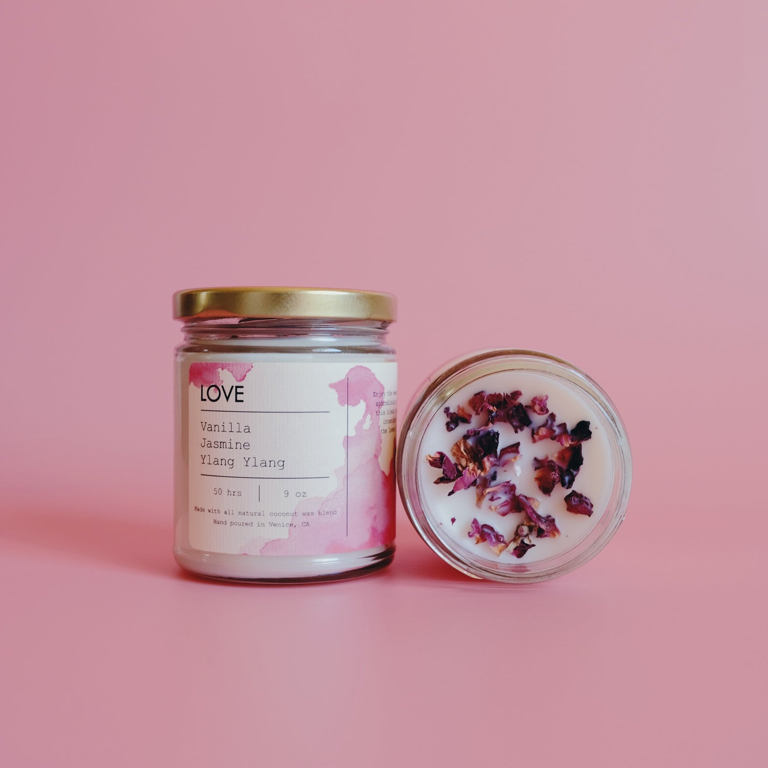Two jars on pink background; one candle upright, the other open with dried flowers on top.