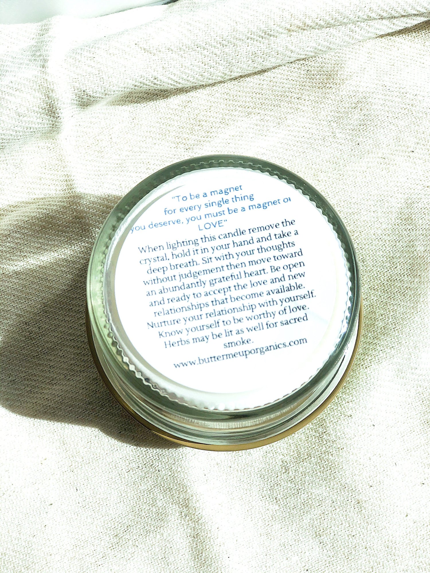 A candle tin on a beige fabric, with text about love and mindfulness on the lid.