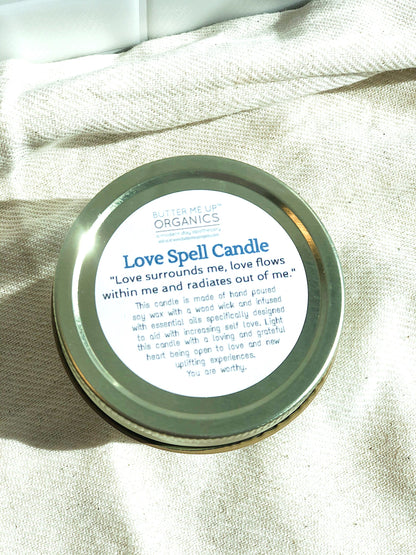 Gold tin candle labeled "Love Spell Candle" on a beige fabric background.