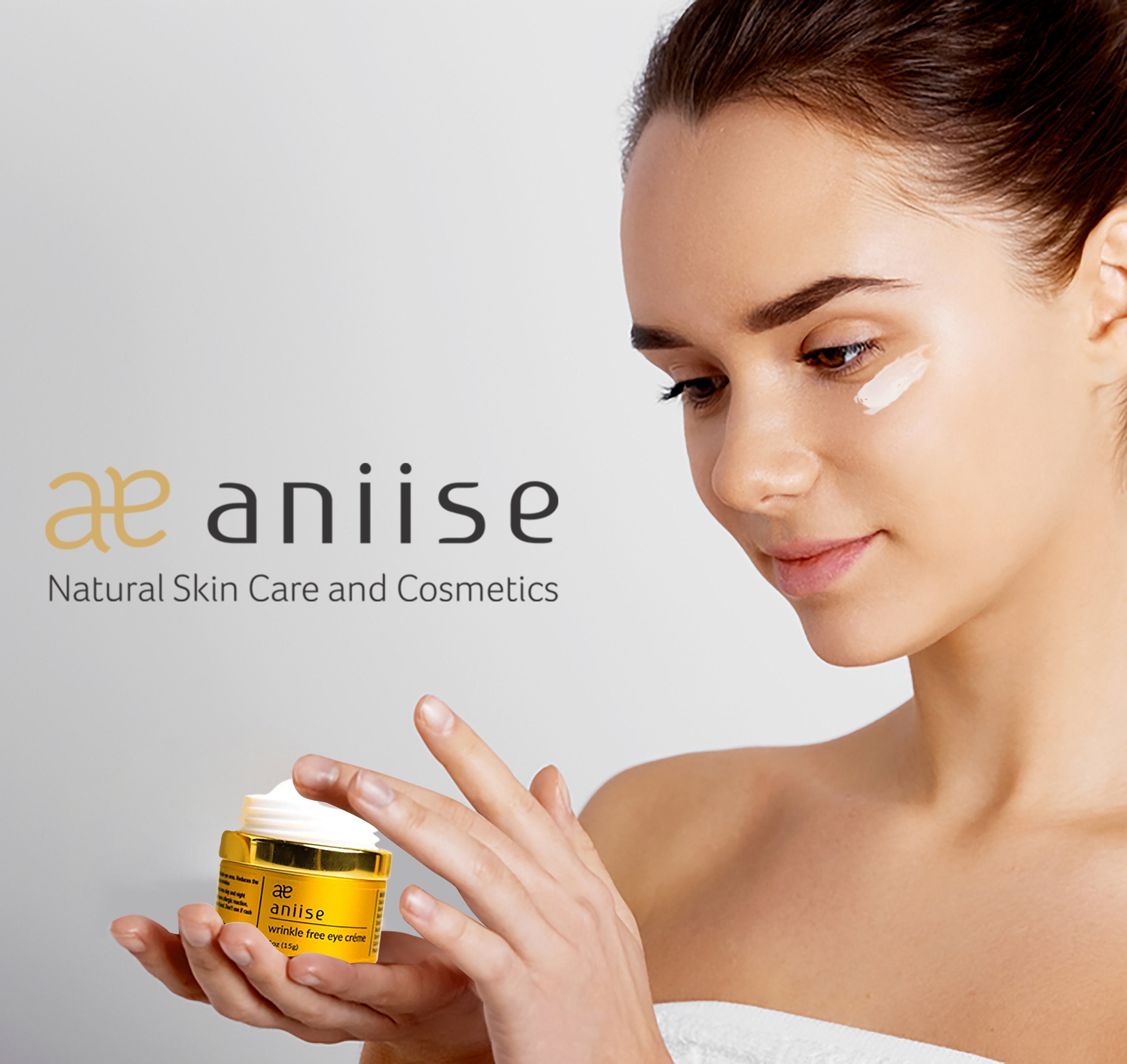 Woman applying eye cream from a yellow jar with "aniise" logo; wearing white, soft focus.