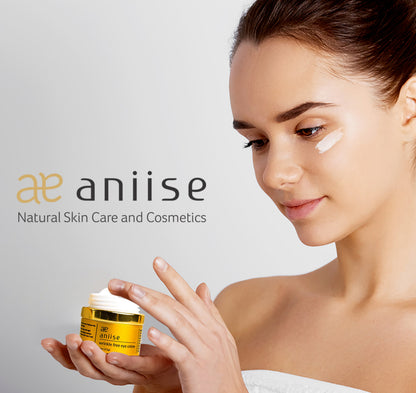 Woman applying eye cream from a yellow jar with "aniise" logo; wearing white, soft focus.