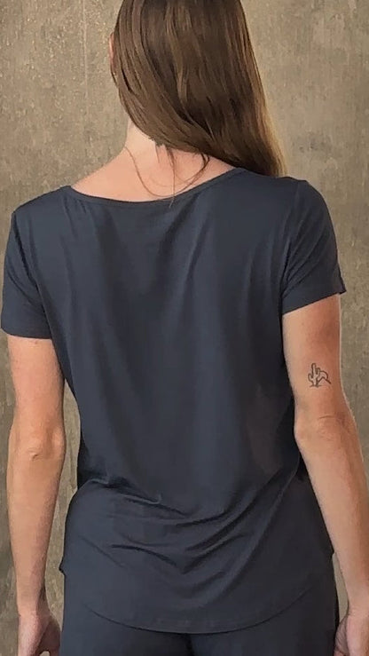 Person with long hair, wearing navy shirt and pants, showing small tattoo on left forearm.