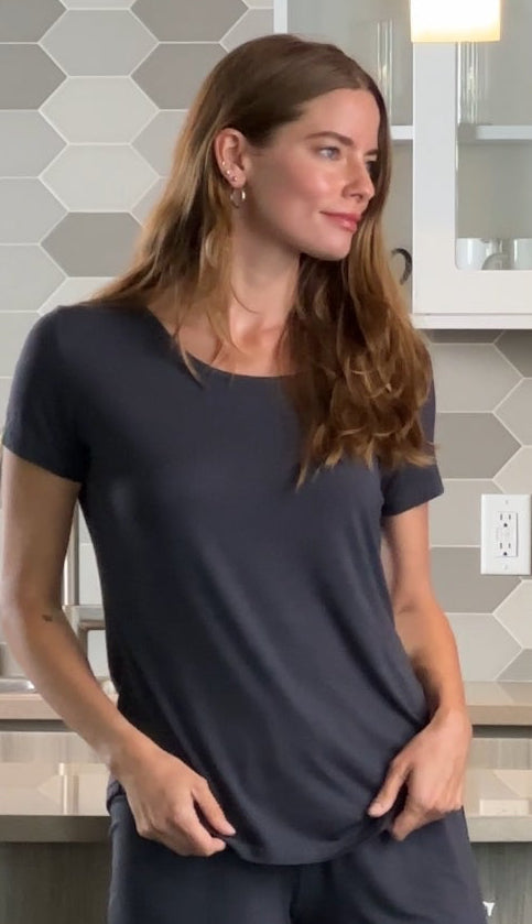 Woman with long brown hair in dark shirt against hexagonal tile wall background.